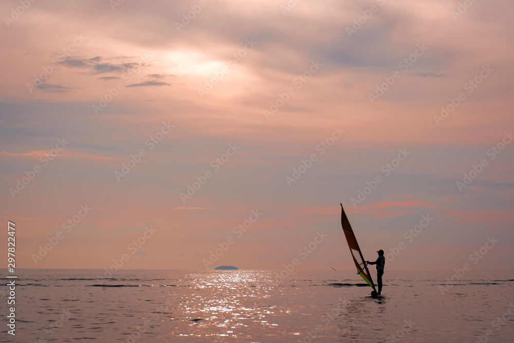 Naklejka premium A woman sailing on a windsurfing board while on the sea in the evening.