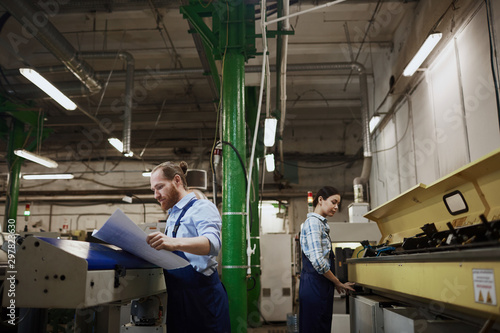 Two manual workers in overalls busy with their work on lathes in printing plant