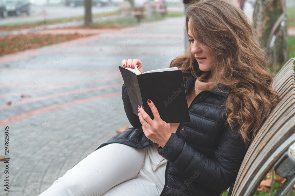 Obraz premium Girl holds book in her hands. The girl sitting on a bench, reading a book.