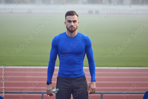 A male athlete in training stands at the stadium in the fog.