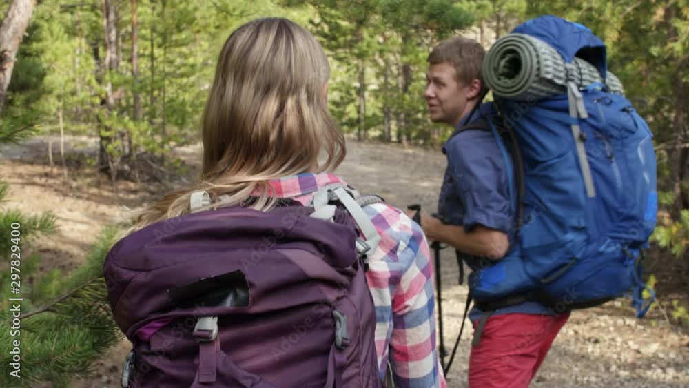 Joyful couple of tourists with rucksacks searching for the place to have rest in forest Joyful couple of tourists with rucksacks searching for the place to have rest in forest