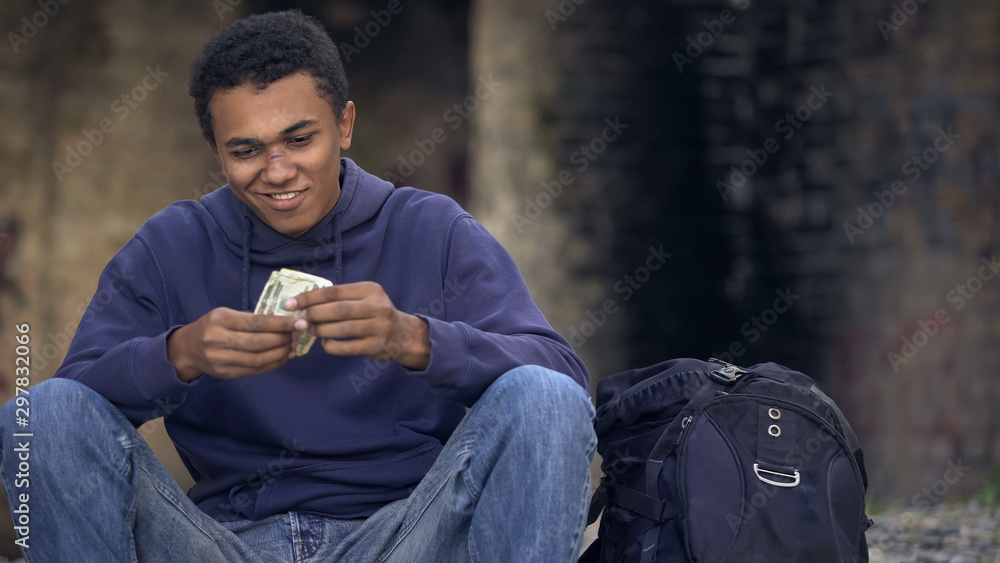Homeless millennial looking at dollars sitting street alone, low living standard Homeless millennial looking at dollars sitting street alone, low living standard