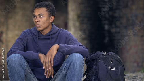 Lonely afro-american teenager sitting in abandoned house and waiting for friends