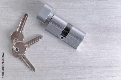 Lock core and door keys on a light background. Repair in the house. Installing a new lock on the door. Spare parts for the door on a gray wooden table.