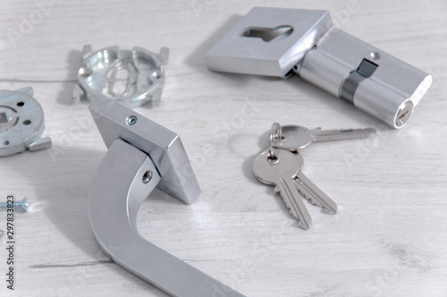 The core of the lock, handles and door keys on a light background. Repair in the house. Installing a new lock on the door. Door hardware and parts on a gray wooden table.