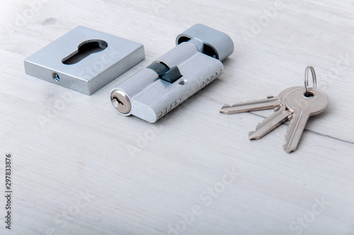 Lock core and door keys on a light background. Repair in the house. Installing a new lock on the door. Spare parts for the door on a gray wooden table.