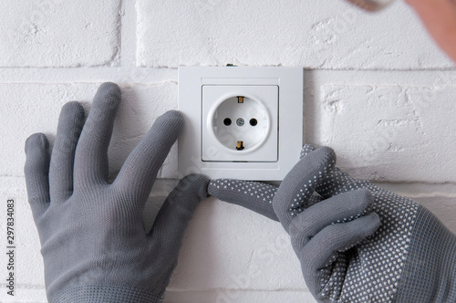 The guy installs new sockets. Repair in the house. The guy twists the screws on the sockets with a screwdriver. Rosette on a white loft background.