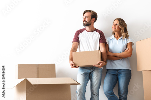 Photo of smiling couple looking aside and holding cardboard box