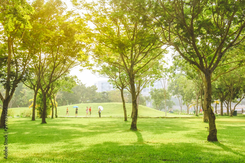 People are walking under beautiful pure sunrise morning in public park with green grass, tree and flower. Half moon park in Ho Chi Minh city, Vietnam.
