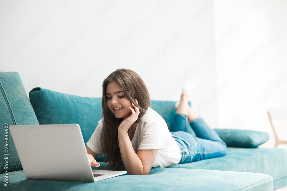cute young woman having online conversation on her laptop lying on the sofa