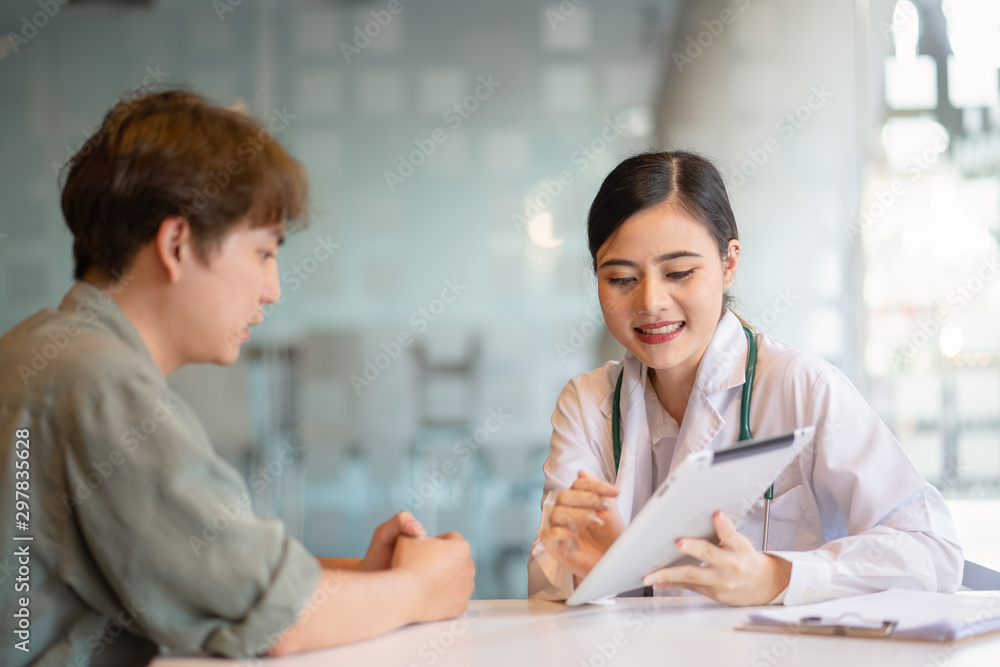 Fototapeta premium Asian woman doctor talking with male patient in doctors office.