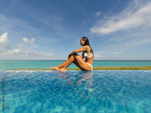 Beautiful young woman sitting by swimming pool and enjoying by poolside