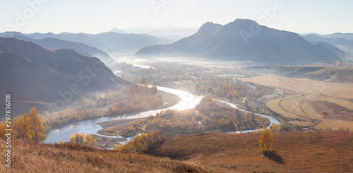 Beautiful autumn view. Charysh River in the Altai Mountains. Reflection of the sun in the waters of the river, soft light, morning haze.