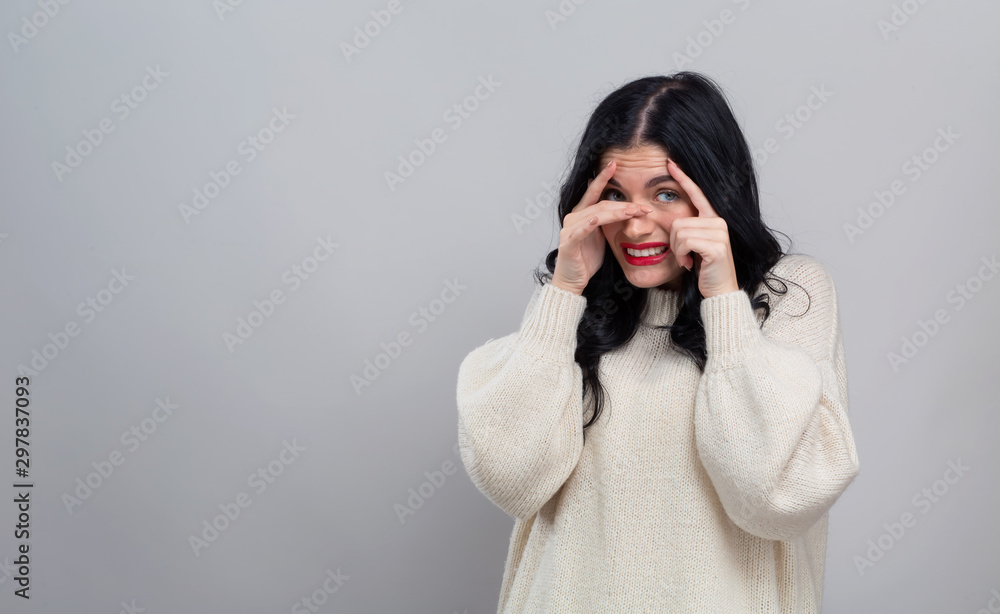 Young woman peeking though her fingers on a gray background Young woman peeking though her fingers on a gray background
