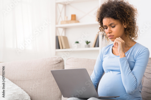 Pensive pregnant woman using laptop at home