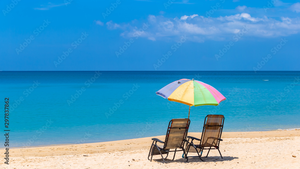 Pair of sun loungers and a beach umbrella on a deserted beach, Beach umbrella on a sunny day, sea in background.