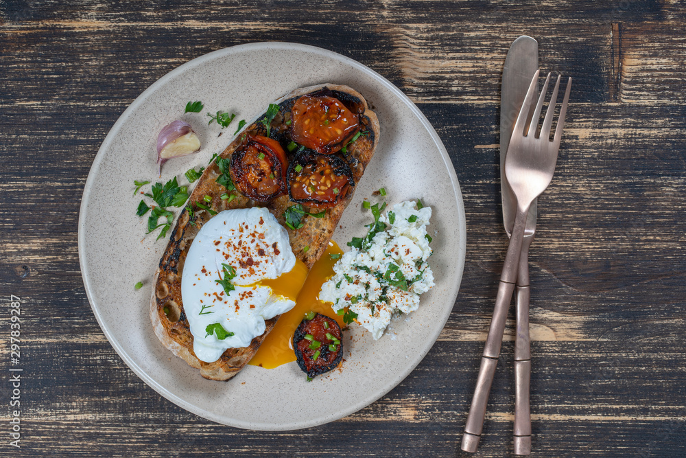 Poached egg on a piece of bread with fried red tomato, garlic and cottage cheese on a plate, close up Poached egg on a piece of bread with fried red tomato, garlic and cottage cheese on a plate, close up