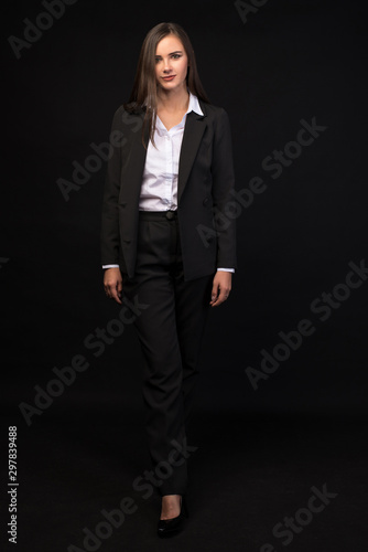a young beautiful girl in a full-length business suit on a black background, a beautiful brunette in a jacket and black pants, long straight dark hair