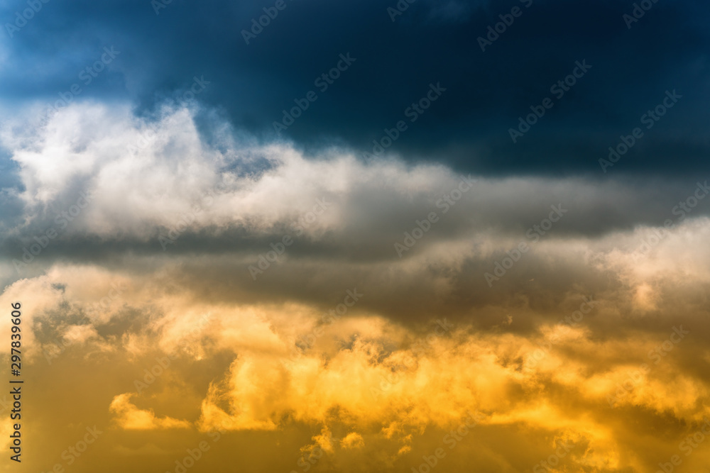 Dramatic blue thunderclouds on top and yellow-golden fluffy clouds illuminated by rays of sun on below. Stunning view natural meteorology background. Amazing cloudscape to weather change before rain. Dramatic blue thunderclouds on top and yellow-golden fluffy clouds illuminated by rays of sun on below. Stunning view natural meteorology background. Amazing cloudscape to weather change before rain.