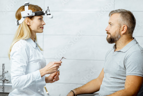 Otolaryngologist preparing for the medical examination procedure to an adult man, holding larynx tools at the ENT office