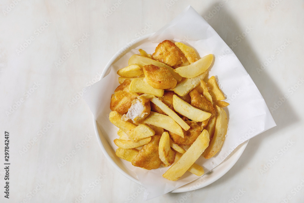 Classic british fast food fish and chips served on white paper in plate over white marble background. Flat lay, space Classic british fast food fish and chips served on white paper in plate over white marble background. Flat lay, space