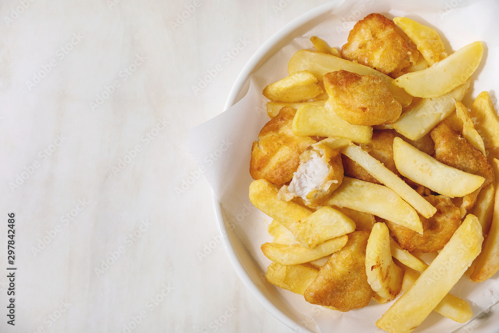 Classic british fast food fish and chips served on white paper in plate over white marble background. Flat lay, space Classic british fast food fish and chips served on white paper in plate over white marble background. Flat lay, space