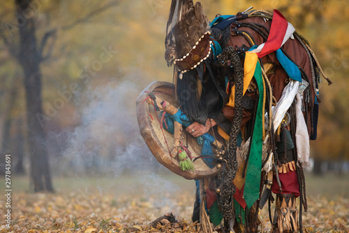 Mongolian traditional shaman performing a traditional shamanistic ritual with a drum and smoke in a forest during autumn afternoon. Ulaanbaatar, Mongolia. photo