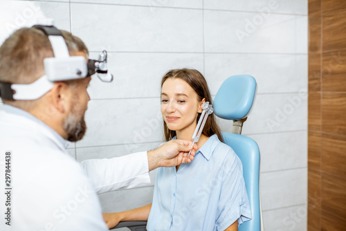 Billede på lærred Senior otolaryngologist examining ears with ENT tuning fork for a young patient in the medical office