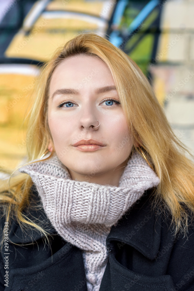 Millennial girl with nose ring and turtleneck sweater looking at camera in front of a graffiti wall background Millennial girl with nose ring and turtleneck sweater looking at camera in front of a graffiti wall background