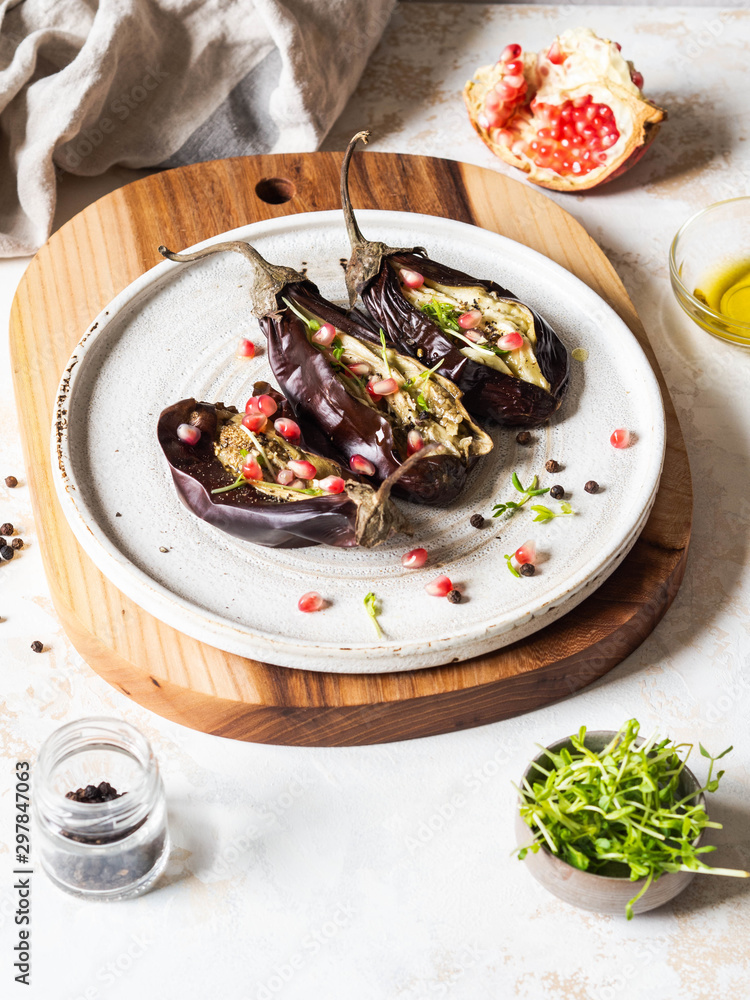 Baked eggplants slices with spices, sprouts, pomegranate and olive oil on a white ceramic plate on a gray background.