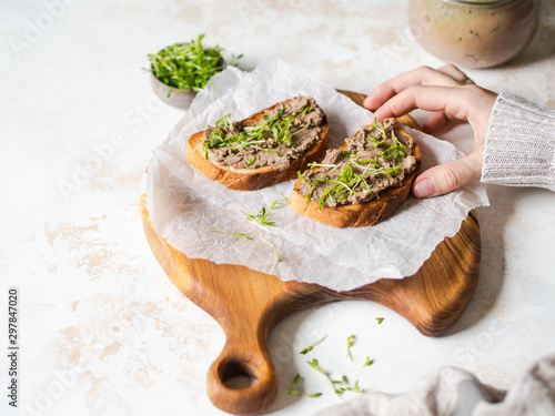 Two toasts chicken rillettes (pate) on white bread with sprouts on a wood cutting board and female hand takes toast on marble background. Copy space photo