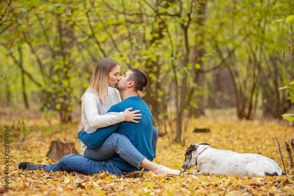 Fototapeta premium Portrait of young happy couple with cute dog kissing in autumn park