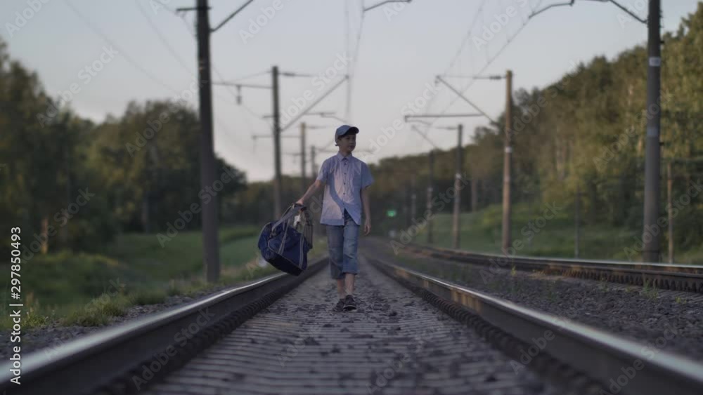 funny boy with a travel bag goes by rail, outdoors funny boy with a travel bag goes by rail, outdoors