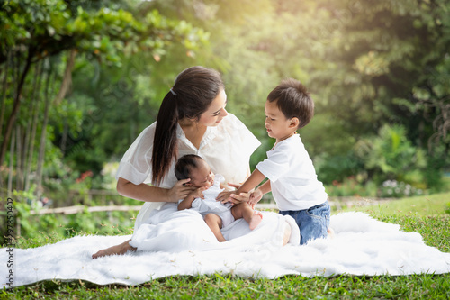 Beautiful Asian young mother  or single mom with new born baby girl and son are doing activities and relaxing in the park. concept of duties of wife and mother in raising children and family. © amornchaijj