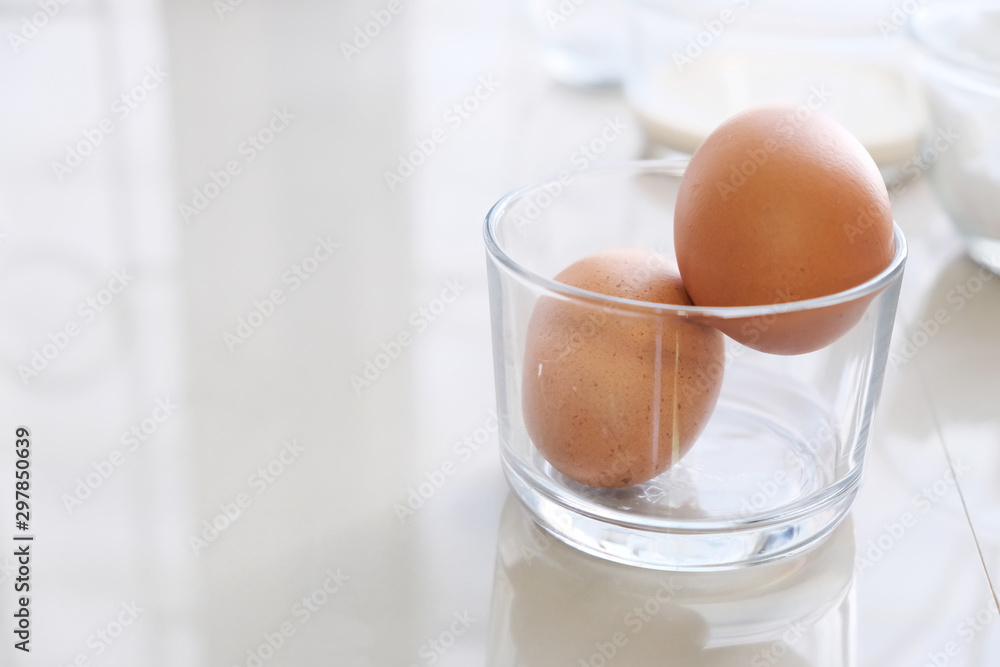 Two organic chicken eggs are placed in a clear glass on the white table. Two organic chicken eggs are placed in a clear glass on the white table.