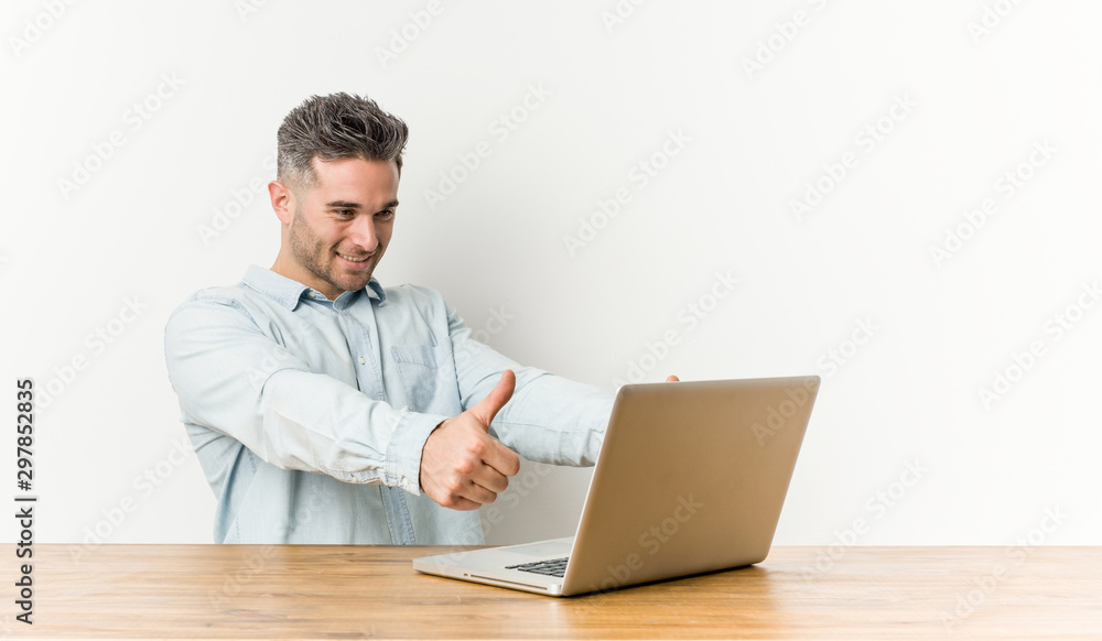 Young handsome man working with his laptop with thumbs ups, cheers about something, support and respect concept. Young handsome man working with his laptop with thumbs ups, cheers about something, support and respect concept.