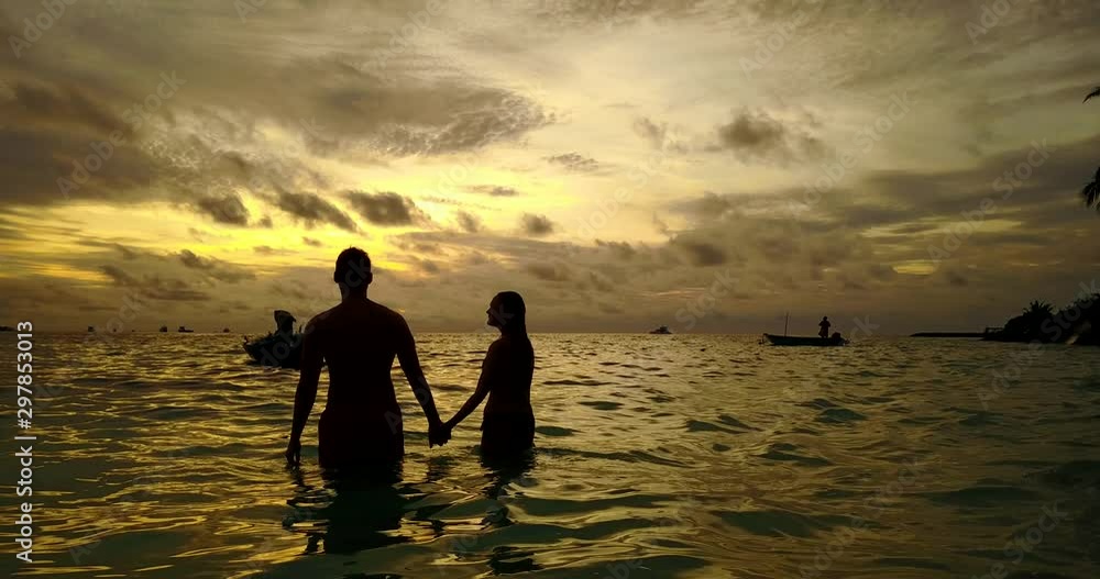 Couple in love watching golden sunset from shallow waters of shore in Pulau Banggi, Malaysia
