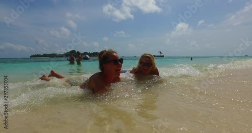 Brunette and blond girls sunbathing on shallow water and washed by waves in paradise island of Babuyan photo