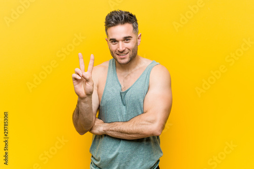 Young fitness man against a yellow background showing number two with fingers.