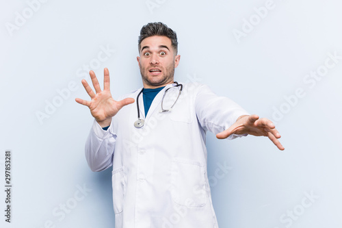 Young handsome doctor man being shocked due to an imminent danger