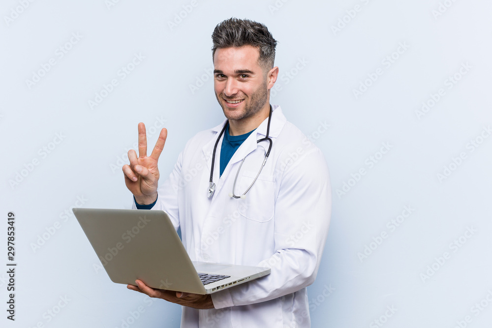 Caucasian doctor man holding a laptop showing victory sign and smiling broadly. Caucasian doctor man holding a laptop showing victory sign and smiling broadly.