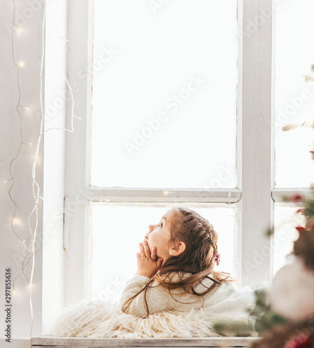 Cute little girl sitting on windowsill on Christmas.