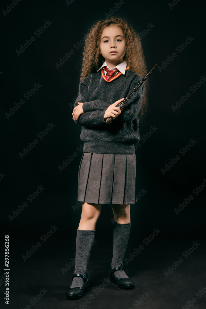 Portrait of a little witch girl with long brown hair dressed in dark clothes, holding magic wand in her hand, posing on black studio background. Portrait of a little witch girl with long brown hair dressed in dark clothes, holding magic wand in her hand, posing on black studio background.
