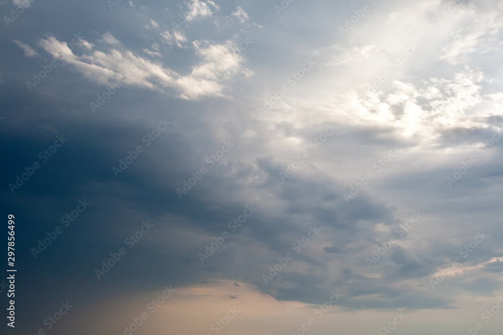 Stormy dramatic dark blue sky with small white clouds and piercing sunlight. Time before the rain background Stormy dramatic dark blue sky with small white clouds and piercing sunlight. Time before the rain background