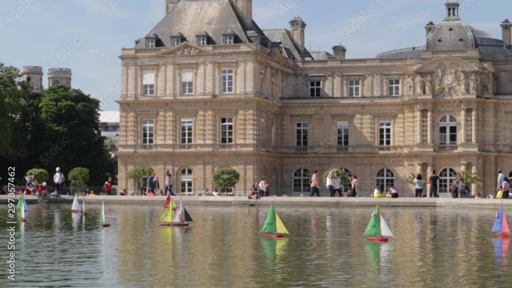 funny view of the toy boat moving in the waters of Luxembourg garden fountain, people walking some are watching in the nearby street. wide shot funny view of the toy boat moving in the waters of Luxembourg garden fountain, people walking some are watching in the nearby street. wide shot