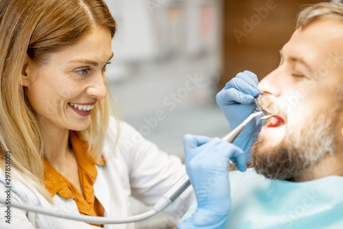 Handsome man as a patient during a teeth inspection with a cheerful female dentist at the dental office, close-up view