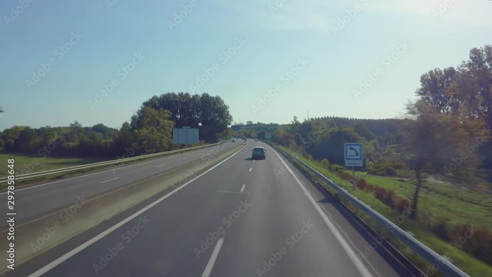 Fly over a highway covered with the greenery including trees and green fields, passing the street signs and fast driven cars on both sides of the road. Fly over a highway covered with the greenery including trees and green fields, passing the street signs and fast driven cars on both sides of the road.