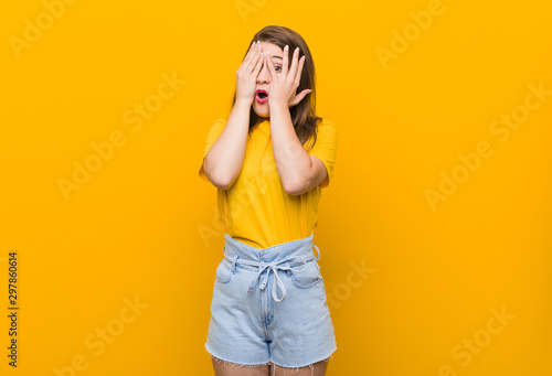 Young woman teenager wearing a yellow shirt blink through fingers frightened and nervous.