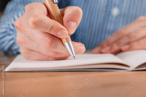 Beautiful Female hands write pen in a notebook of tasks and goals to work on a wooden table