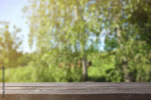  Image of grey wooden table in front of abstract blurred background of trees on a green meadow